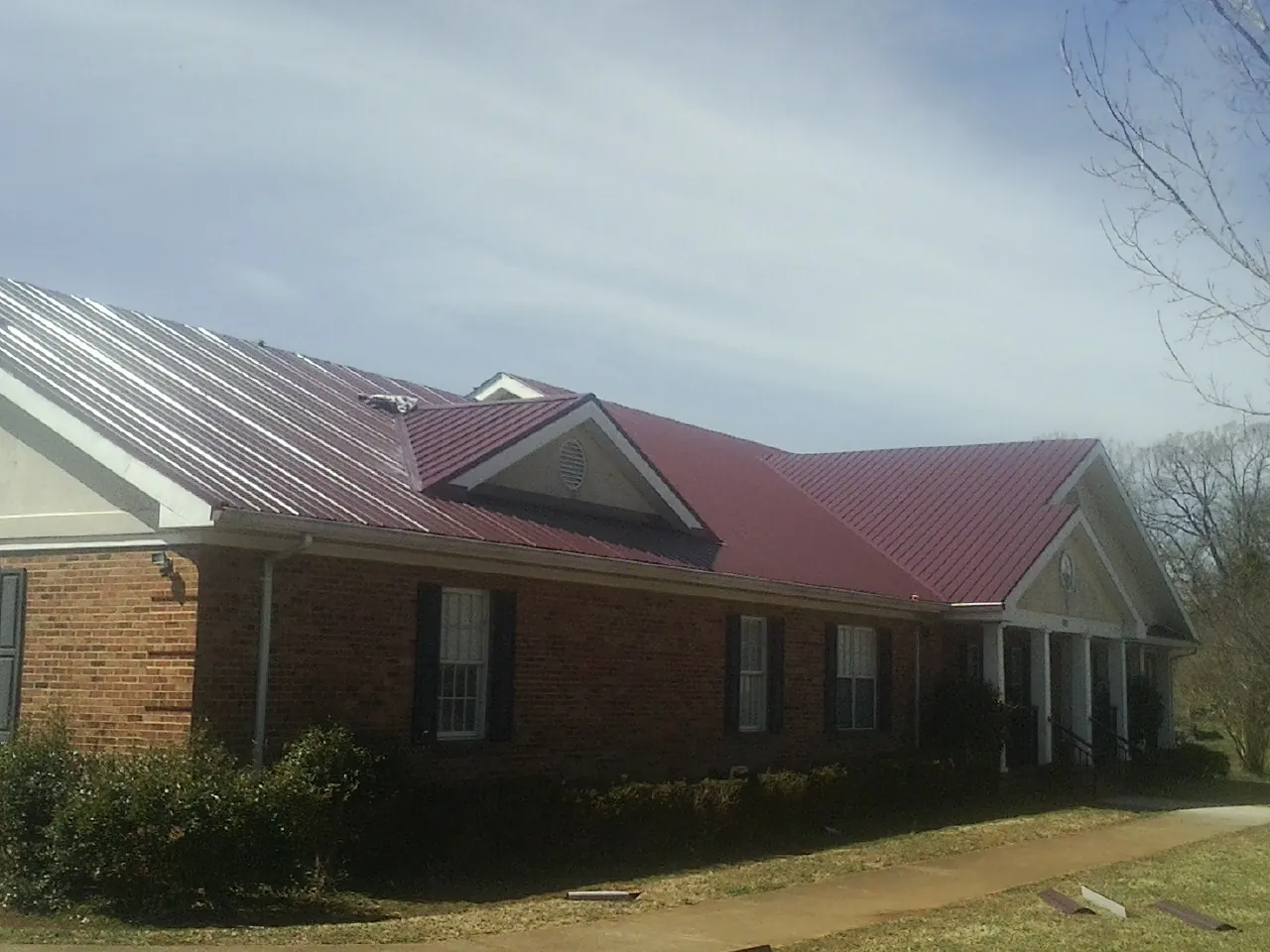 Red metal roof with gabled entries on a long brick building, from a Hail Damage Roof Repair job in Tryon