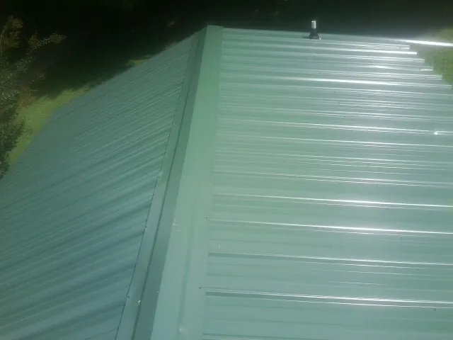 New green metal panels meeting at the ridge of a roof — Flat Roof Repair work by our crew in Tryon